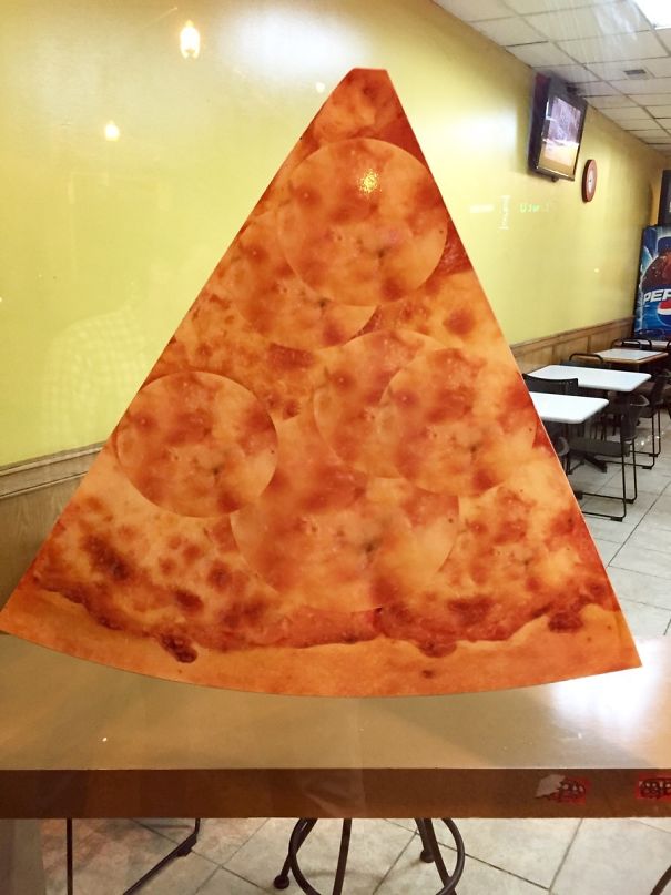 Large slice of pizza with duplicated pepperoni circles showing a hilarious and disastrous Photoshop fail in a restaurant setting.