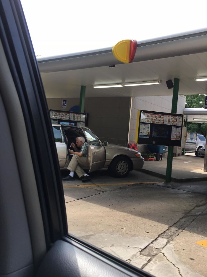 An Elderly Man Sitting Outside Of His Car Door Spoon Feeding His Wife Ice Cream