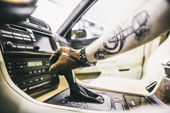 Arm with a tattoo gripping a car gear shift, showcasing a unique tattoo design inside a vehicle.