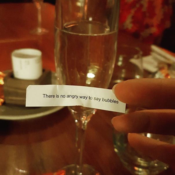 Close-up of a sassy fortune cookie saying, "There is no angry way to say bubbles," next to a glass of champagne.