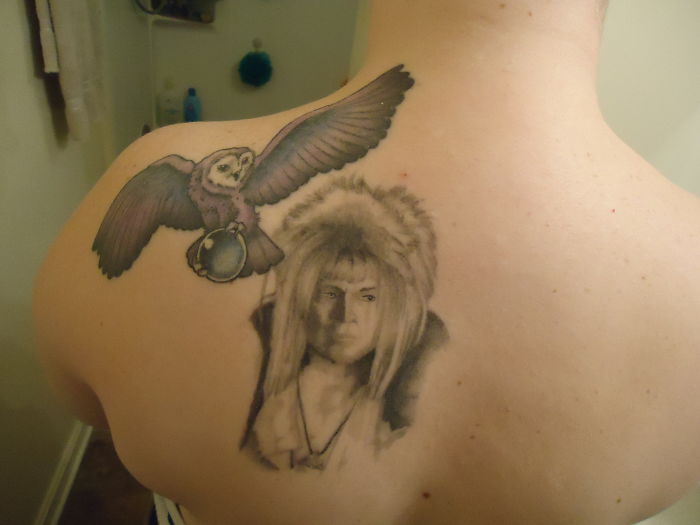 Tattoo of a flying owl with a crystal ball above a portrait on a person's shoulder, showcasing personal tattoo stories.