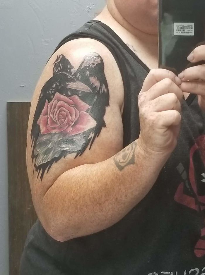 Arm tattoo featuring a black bird and pink rose, reflecting a personal story behind the tattoo design.