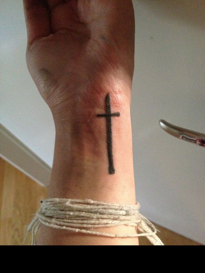 Close-up of a cross tattoo on a wrist, with string wrapped around the arm.