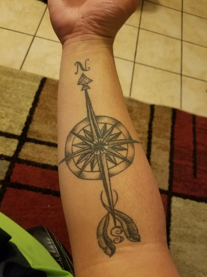 Forearm tattoo of a compass rose with a northern arrow, symbolizing direction and guidance.