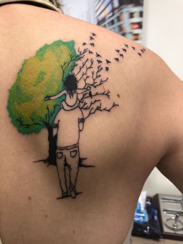 Tattoo of a person carrying a child on their shoulders beside a tree transforming into birds.