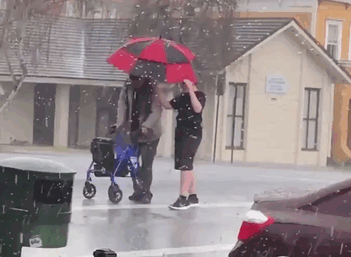 14 Year Old Boy With Umbrella Helps An Elder Cross The Street During A Hailstorm In Vallejo, California Usa