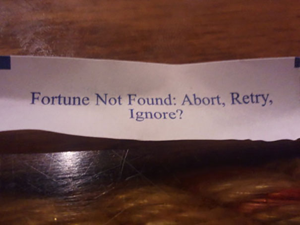 Sassy fortune cookie message reading "Fortune Not Found: Abort, Retry, Ignore?" placed on a wooden table.