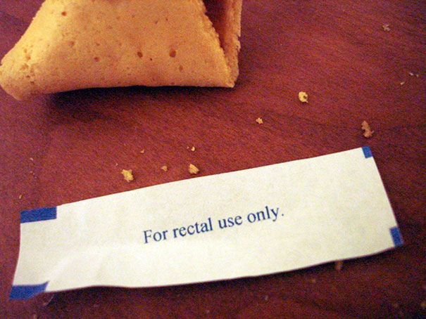 Fortune cookie with a humorous message: "For rectal use only" on a wooden surface.