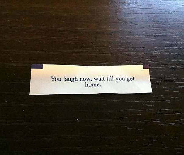 Fortune cookie saying: "You laugh now, wait till you get home" on a wooden table.