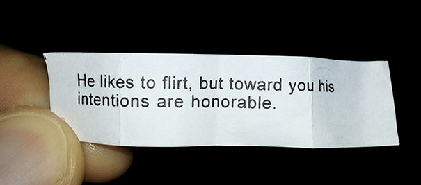 Fortune cookie with a sassy message about flirting intentions, held between fingers.