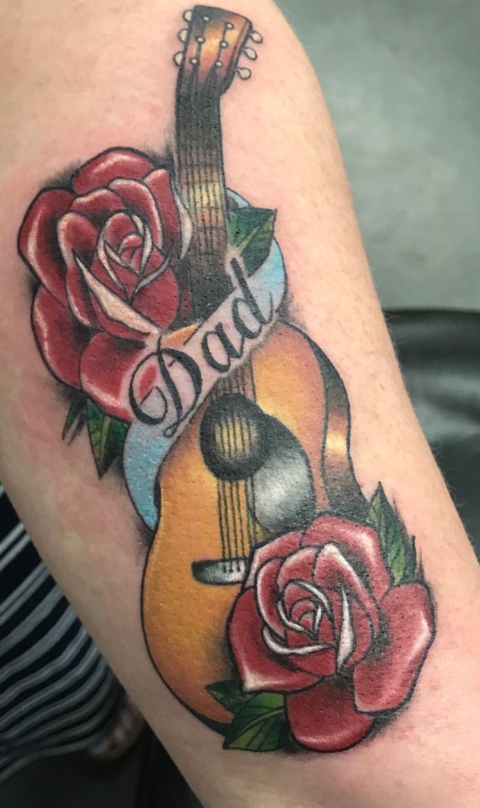 Guitar and roses tattoo with "Dad" banner, symbolizing personal stories behind tattoos.