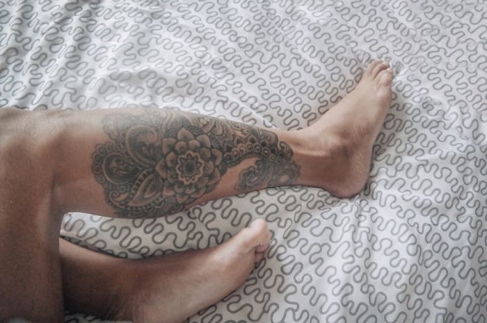 Decorative leg tattoo with intricate patterns on a bedspread.