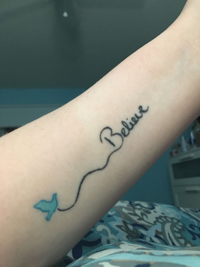 Tattoo of the word "Believe" with a blue butterfly on a person's arm.
