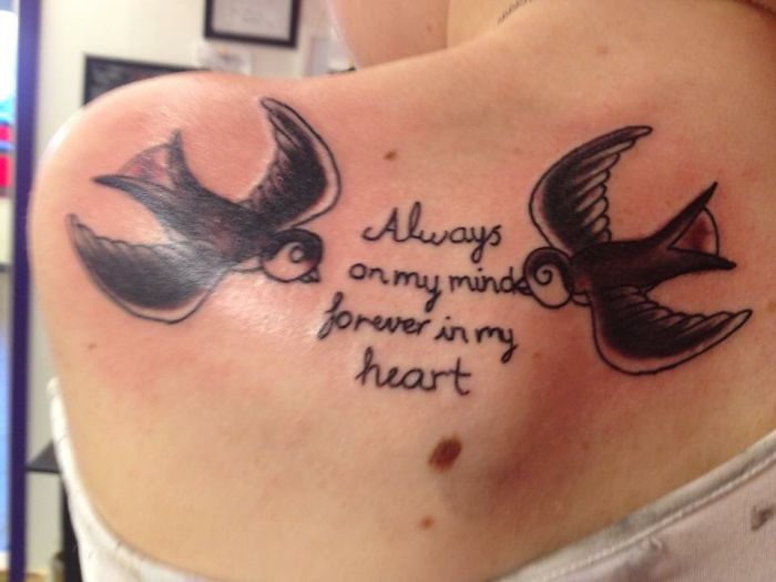 Tattoo of two swallows with the text "Always on my mind, forever in my heart" on a person's upper back.