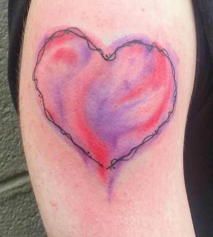 Heart-shaped watercolor tattoo with red and purple hues on skin; creative tattoo art design.