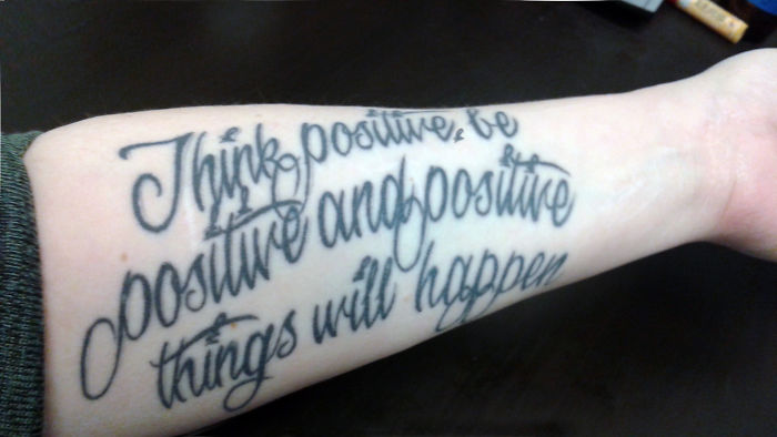 Tattoo reading "Think positive, be positive and positive things will happen" on a forearm.
