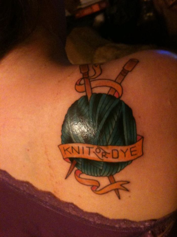 Tattoo of yarn with knitting needles and a banner reading "Knit or Dye" on shoulder.