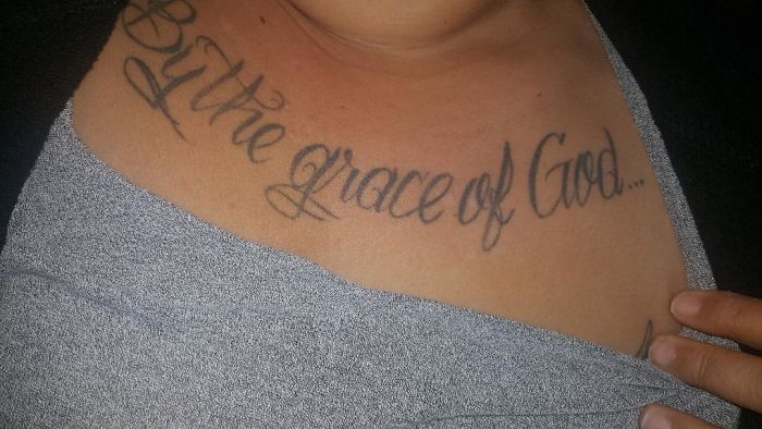 Chest tattoo with the phrase "By the grace of God" in elegant script on a person's skin.