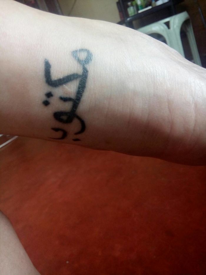 Tattoo on forearm featuring stylized text, with a unique design, in a warm indoor setting.