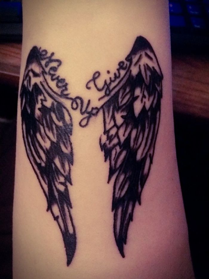 Tattoo of angel wings with "Never Give Up" text on a forearm, showcasing unique tattoo stories.