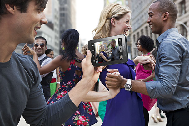 A group of people dancing outdoors while one person captures the moment on a smartphone in a lively setting.
