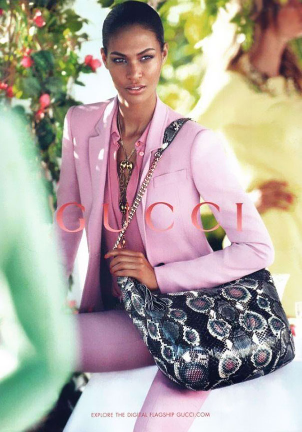 Model in a pink suit holding a patterned handbag with visible Photoshop fails in a fashion advertisement setting.