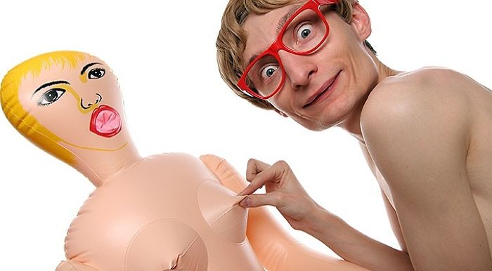 Naked young man with red glasses plays with rubber s*x doll