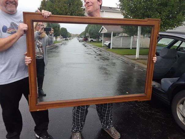 People holding a large mirror on a rainy street, capturing reflections and creating an amusing visual effect.