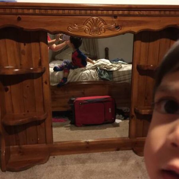 Child's reflection in a mirror with a decorative wooden frame, capturing a playful moment in the room.