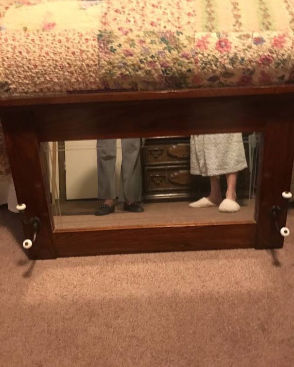 People's feet reflected in a mirror for sale, placed under a quilted cover.