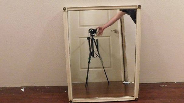 Person's arm adjusting camera tripod reflected in a framed mirror for sale, highlighting the challenge of selling mirrors.