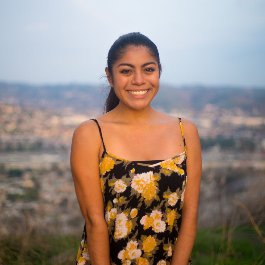 Young woman smiling outdoors during a birthday interview session with a cityscape background at sunset.