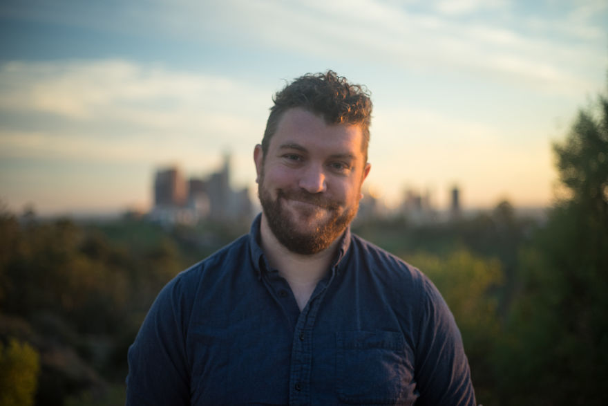 Man standing outdoors at sunset with a city skyline in the background, sharing stories on their birthdays.