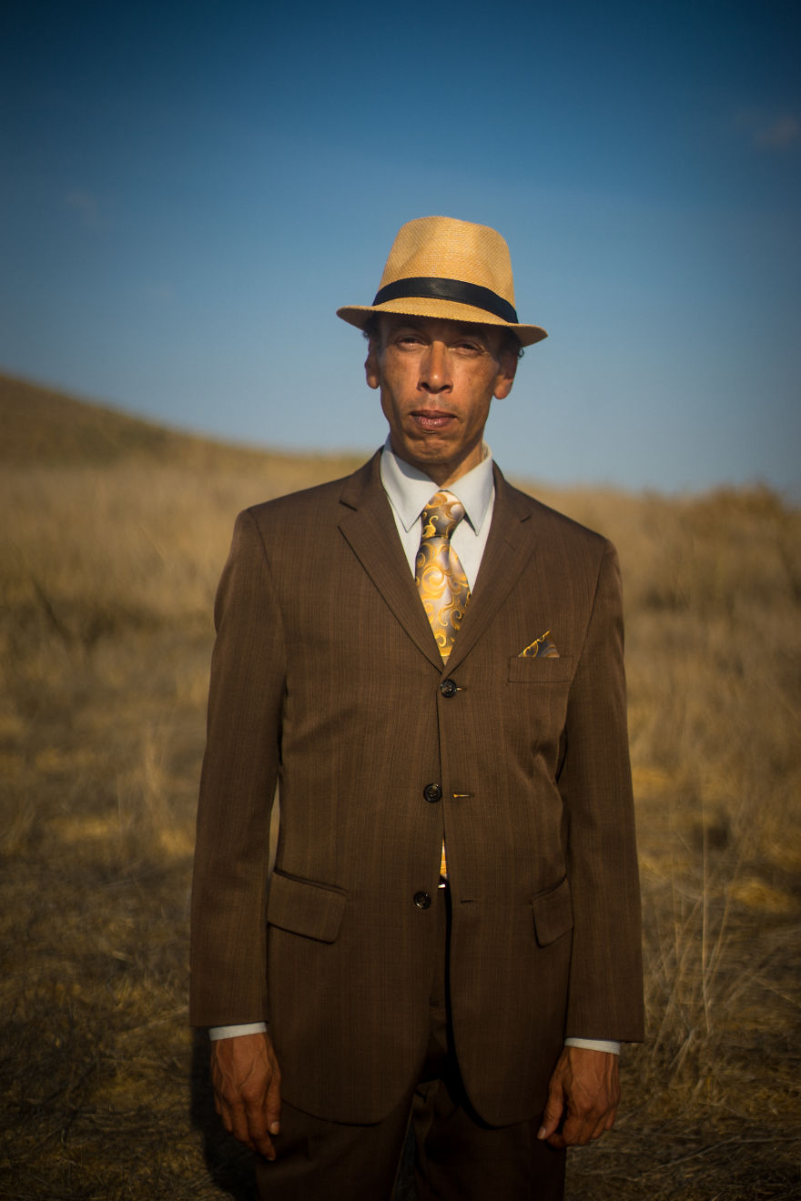 Man in brown suit and fedora standing outdoors in dry grassland, part of interviewing people on their birthdays series.