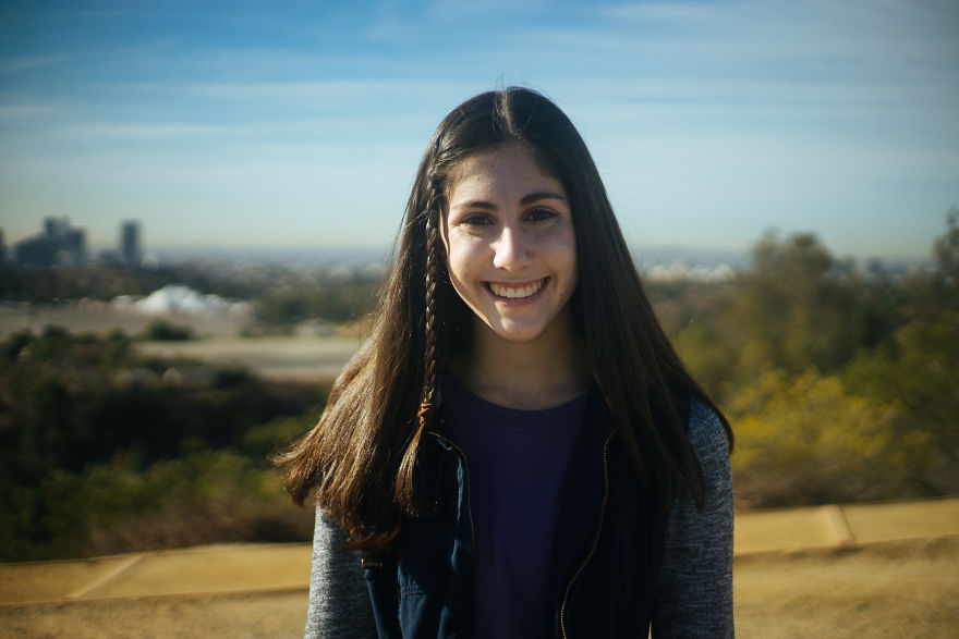 Smiling young woman outdoors with long hair and casual clothes, representing interviewing people on their birthdays.