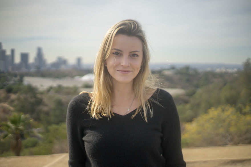 Young woman outdoors with a city skyline in the background, focused on interviewing people on their birthdays.
