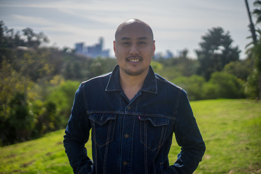 Man wearing denim jacket outdoors, smiling and posing in a park during an interview on their birthday.