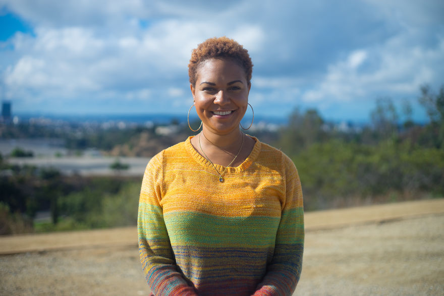 Young woman smiling outdoors, wearing a colorful sweater, representing interviewing people on their birthdays.