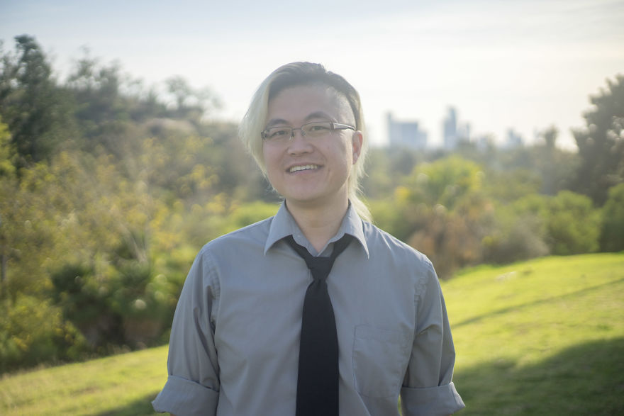 Smiling person with glasses and dyed hair standing outdoors in a park setting, capturing moments of birthday interviews.