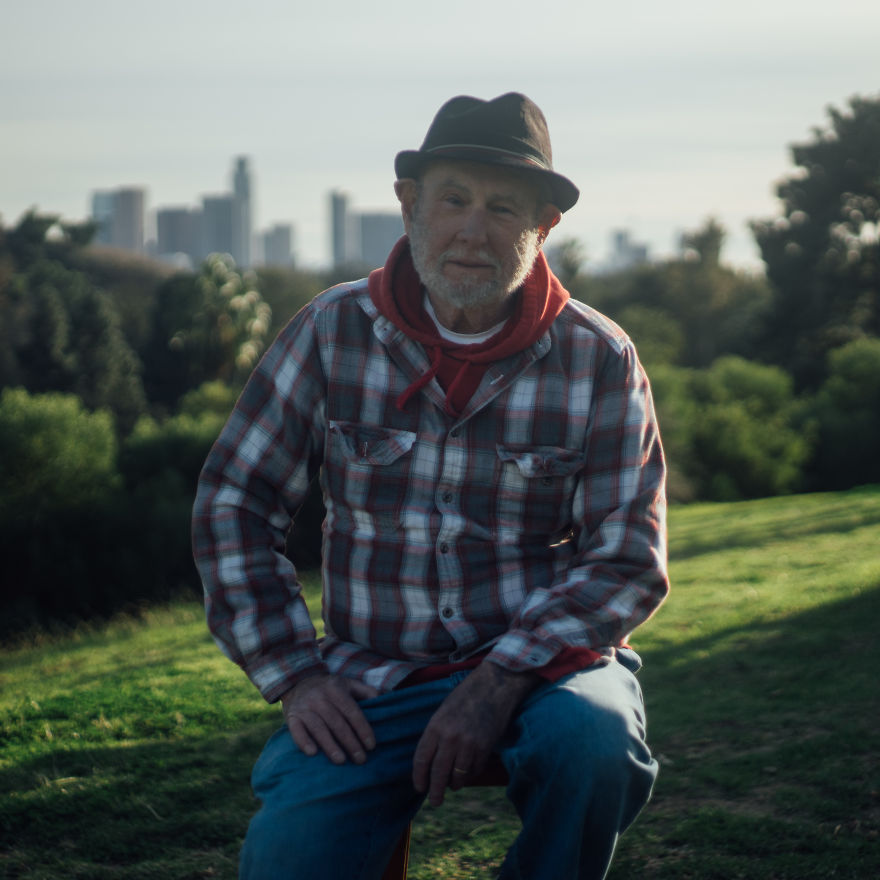 Elderly man in a hat and plaid shirt sitting outdoors, part of interviews with people on their birthdays.