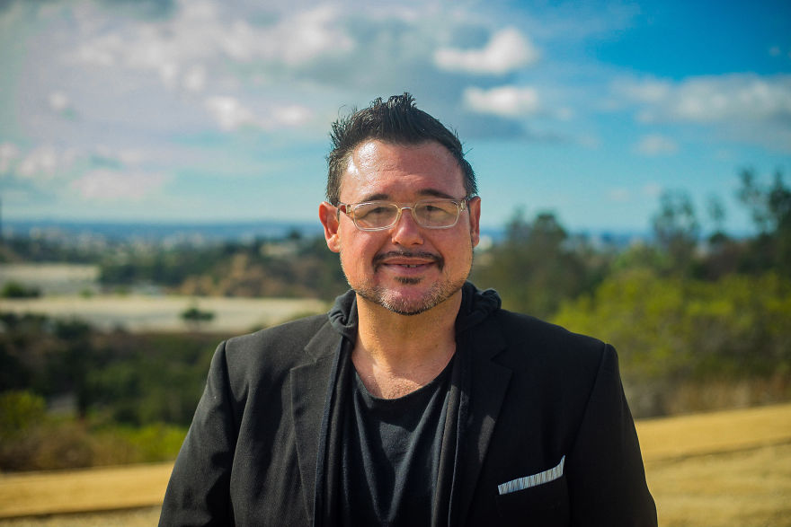 Man wearing glasses and a black jacket smiling outdoors, preparing for interviews about birthdays and personal stories.