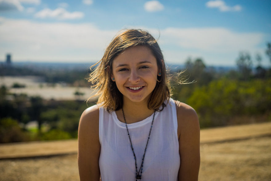 Young woman smiling outdoors on a sunny day, participating in interviews about birthdays and personal stories.