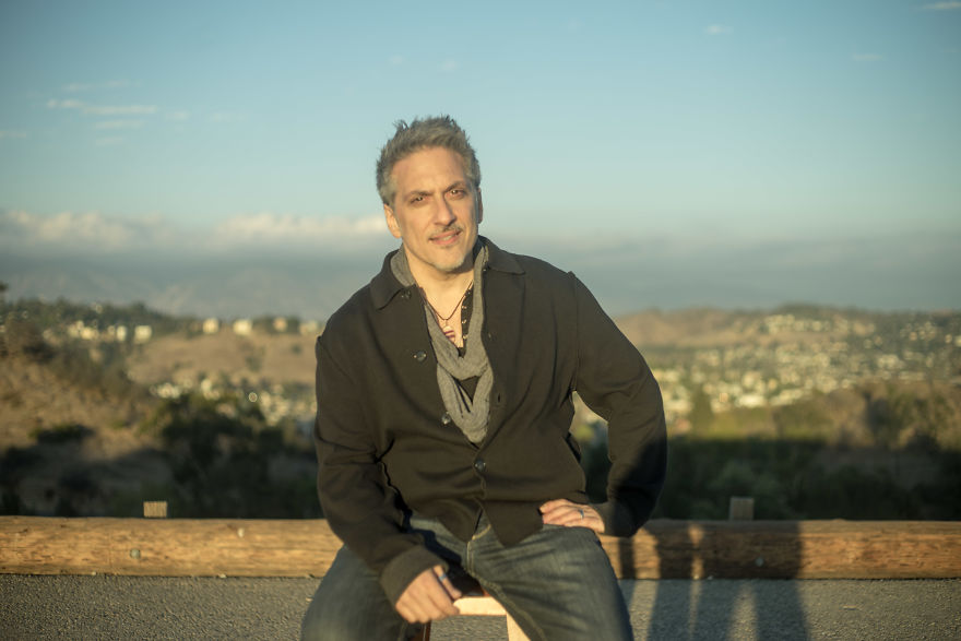 Man sitting outdoors on a bench at sunset, wearing a black jacket, related to interviewing people on their birthdays.