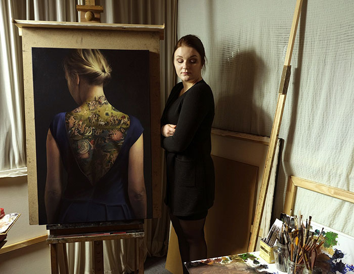 Artist poses with painting featuring intricate back tattoo art inspired by Bosch's "Garden of Earthly Delights. Artist poses with painting featuring intricate back tattoo art inspired by Bosch's "Garden of Earthly Delights.