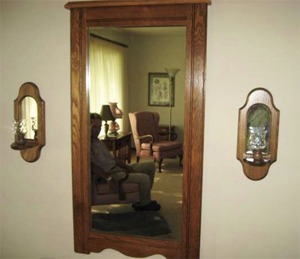 Person reflected in a large wooden-framed mirror, furniture visible in the background, showcasing mirror sales humor.