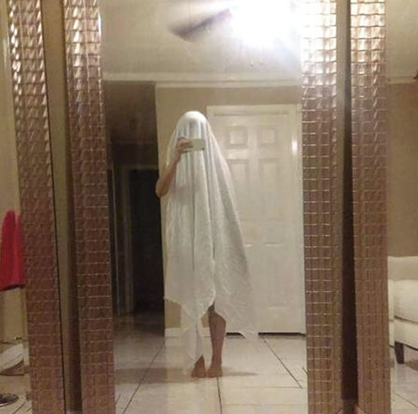 Person covered in white sheet taking a selfie in front of a mirror, reflecting a humorous approach to mirror selling.
