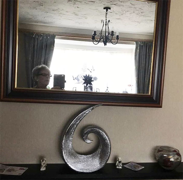 Person attempting to sell a mirror, reflection showing interior with a chandelier and decorative items.