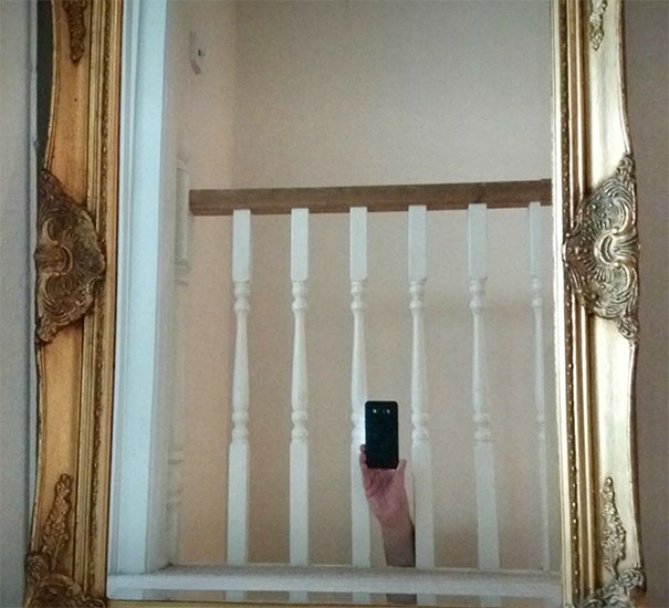 A person taking a photo of a mirror, capturing their hand and phone reflected, with a gold ornate frame.