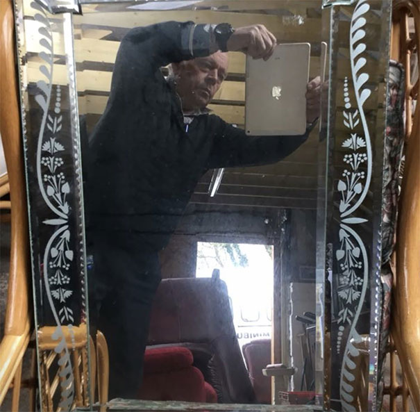 Man taking a photo of a mirror with a tablet, showing the humorous side of selling mirrors.