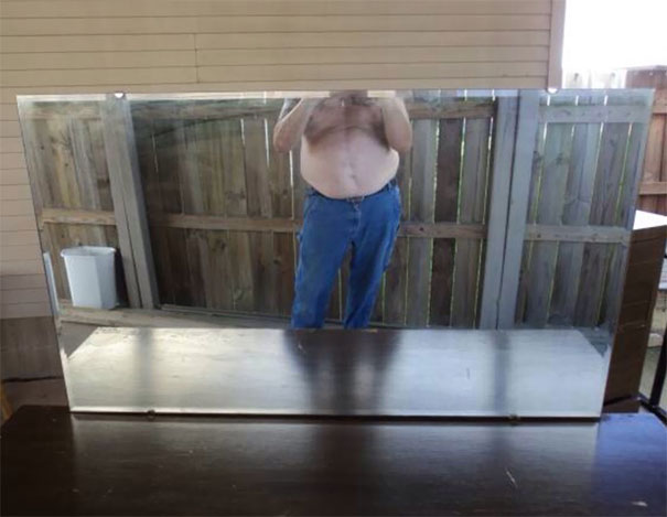 Person reflected in a large mirror, wearing jeans, with a wooden fence in the background, showcasing mirror sale attempts.